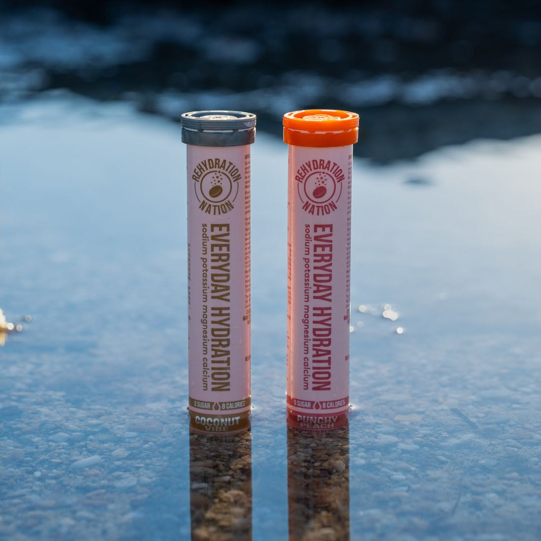 Rehydration Nation Coconut Vibe and Punchy Peach hydration tablets – tubes photographed side by side with reflections in water