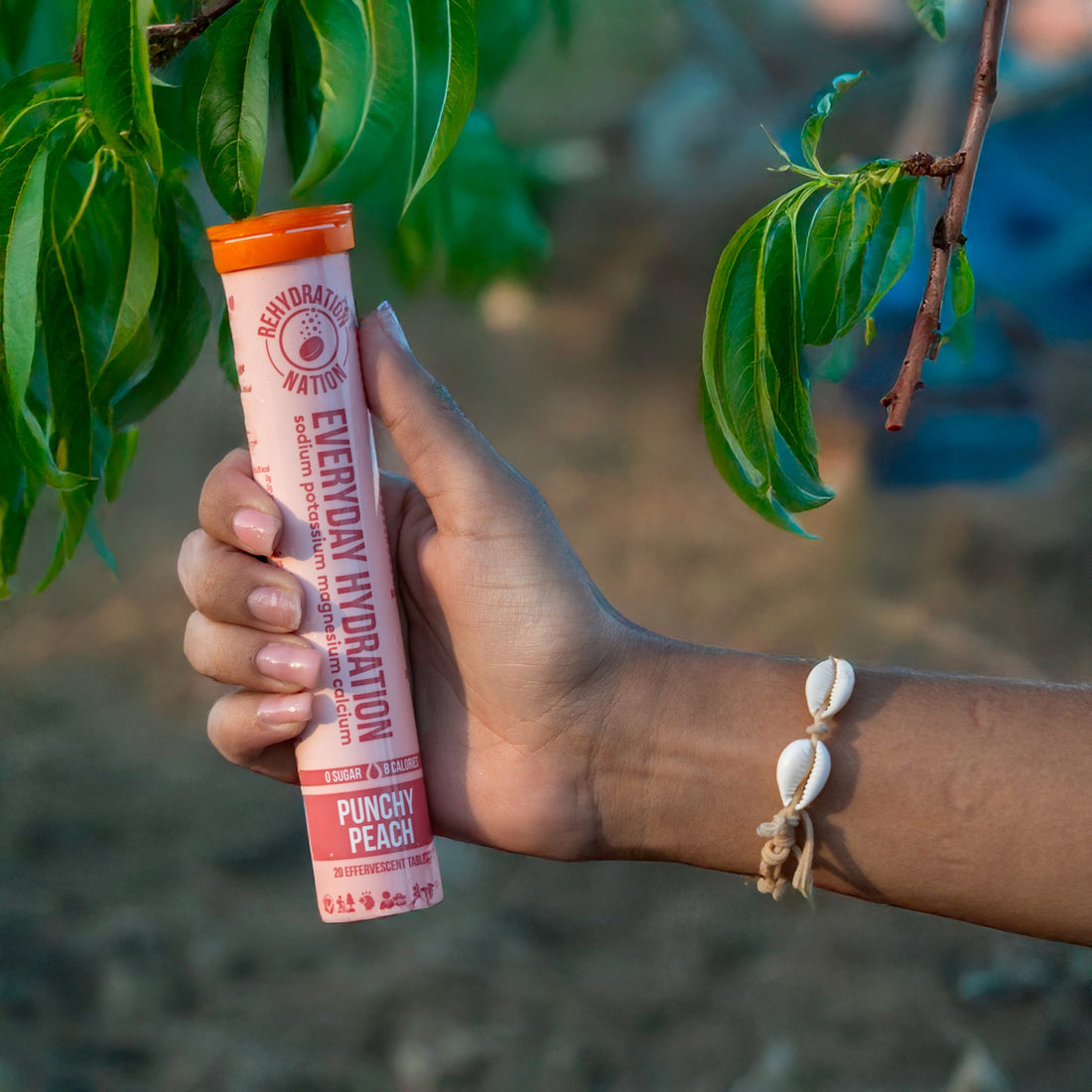 Rehydration Nation Punchy Peach hydration tablets – tube held in hand next to green peach tree leaves outdoors