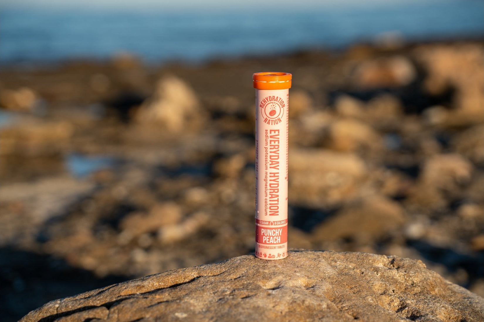 Rehydration Nation Punchy Peach hydration tablets – tube photographed on a rock with sea in the background
