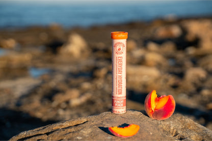 Rehydration Nation Punchy Peach hydration tablets – tube placed on rock with sliced fresh peach by the seaside